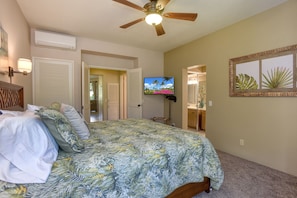 Un dormitorio con cama, ventilador de techo, televisor y obras de arte.