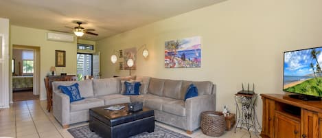 A spacious living room with a large sectional sofa, a coffee table, and a television on a wooden cabinet.