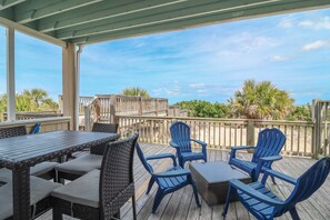 A covered outdoor deck with a wooden table and chairs, overlooking a beach.