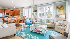 Uma sala de estar ampla com conjunto de jantar, uma poltrona azul e um sofá com almofadas florais.