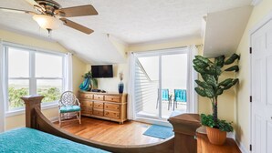 Quarto com teto curvo, mobiliário de madeira, cama com colcha azul, televisão e vista para o exterior através de grandes janelas.
