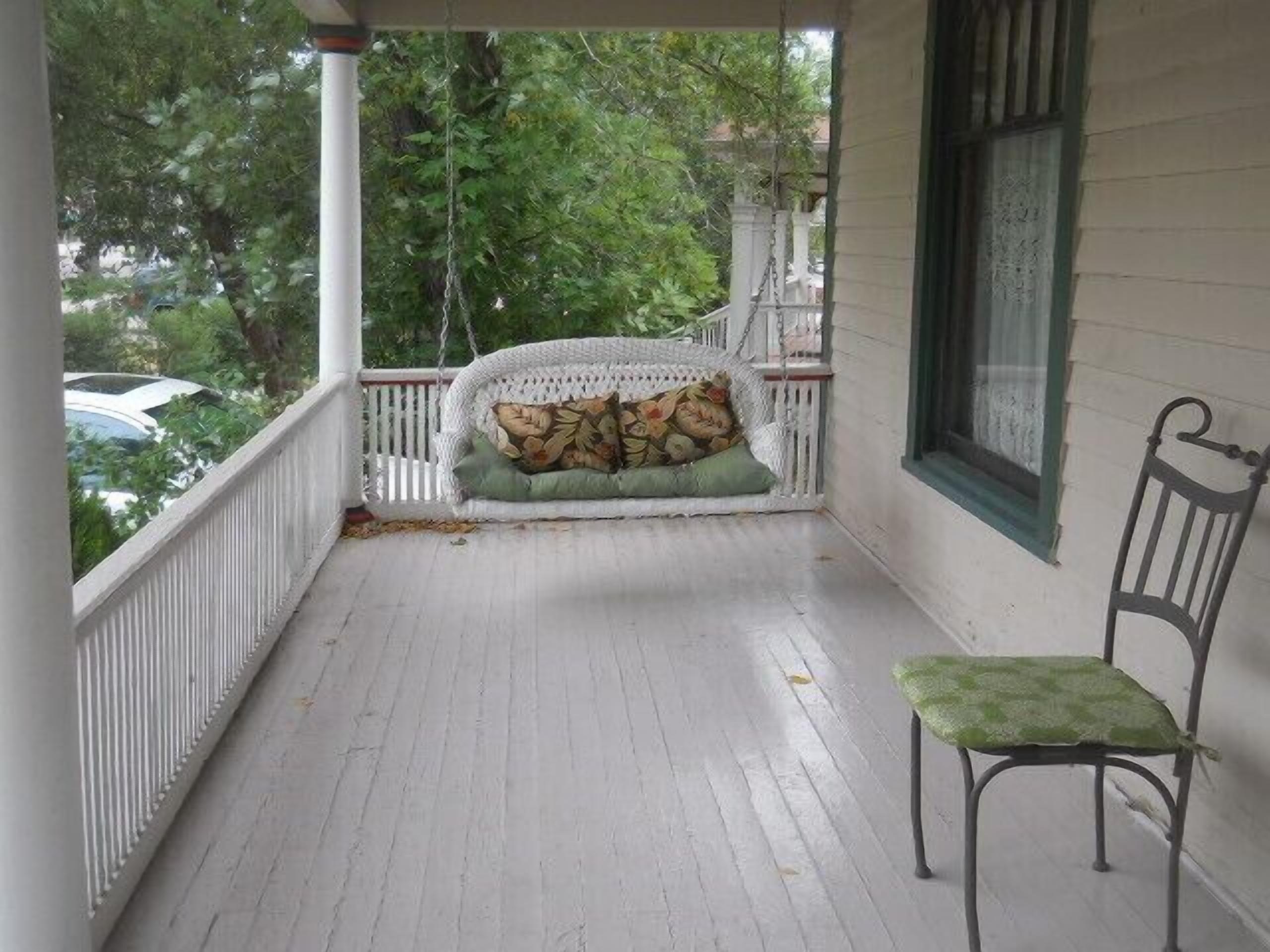 Une véranda avec un banc en osier blanc, un coussin vert et une chaise en métal.