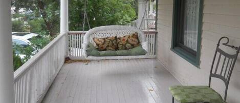 Une véranda avec un banc en osier blanc, un coussin vert et une chaise en métal.