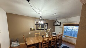 Uma sala de jantar com mesa de madeira, cadeiras, um lustre e uma janela com vista.