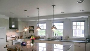 Uma cozinha espaçosa com uma ilha grande, iluminação pendente e vista para o exterior pelas janelas.