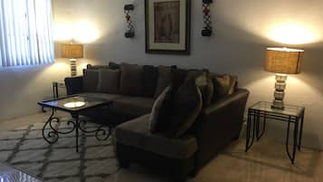 A living room with a sofa, a coffee table, two lamps, a framed picture on the wall, and a patterned rug.