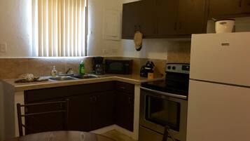 A compact kitchen with dark cabinets, a stainless steel stove, a microwave, and a refrigerator.