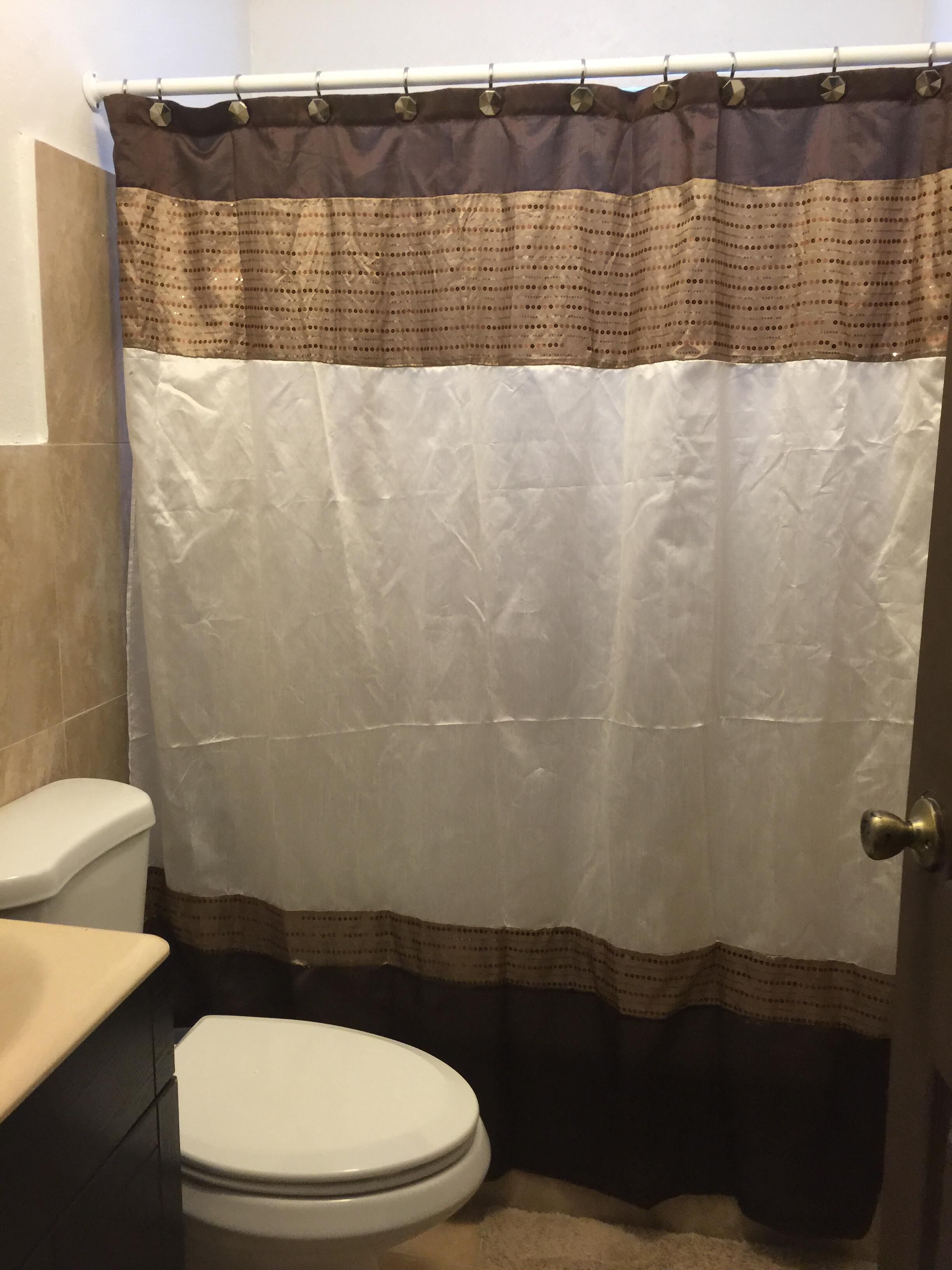 A bathroom with a white toilet, a beige sink, and a shower curtain with a brown and beige pattern.
