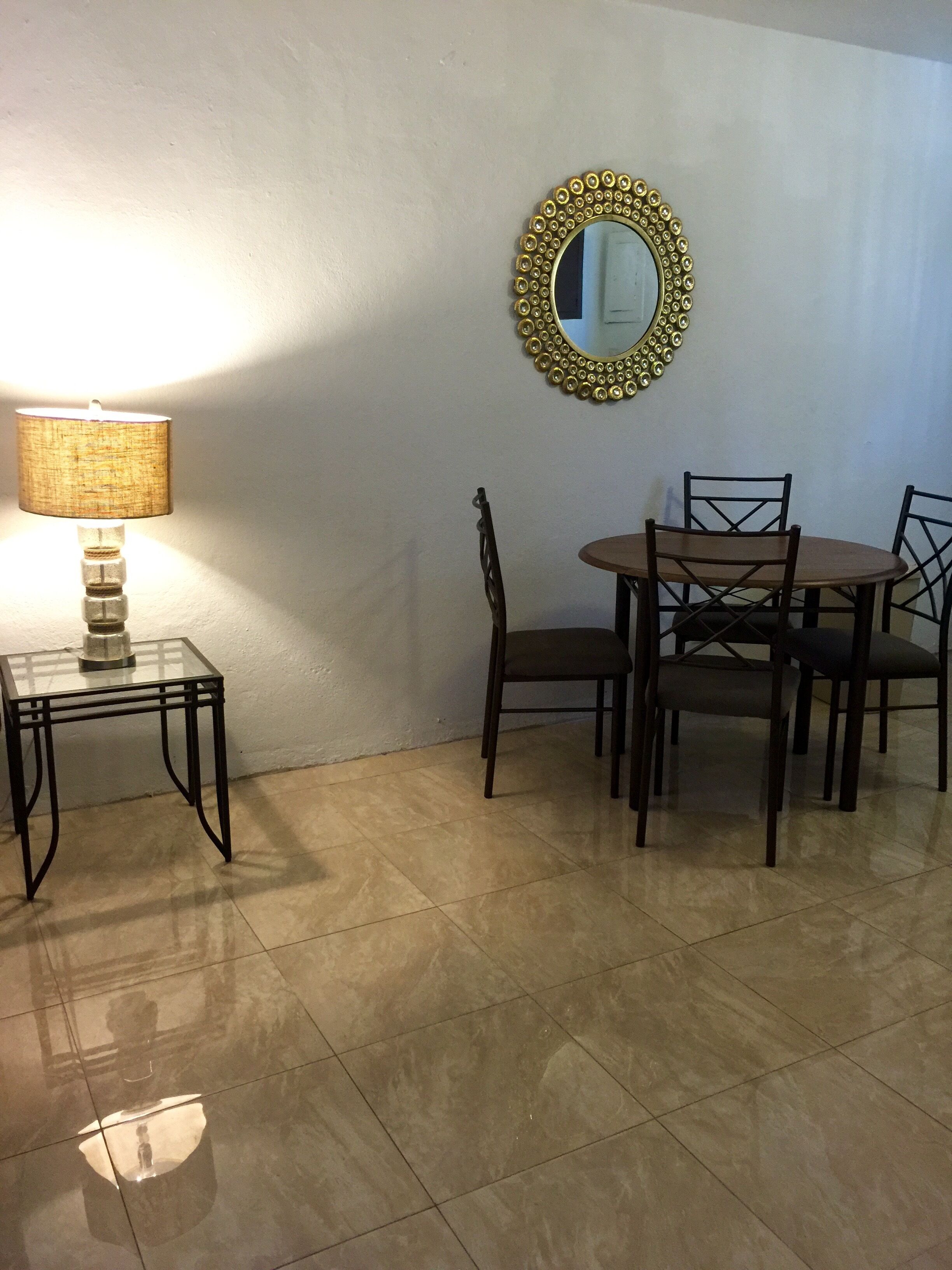 A dining area with a table and chairs, a lamp, and a decorative mirror on the wall.