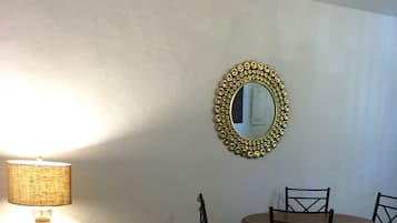 A dining area with a table and chairs, a lamp, and a decorative mirror on the wall.