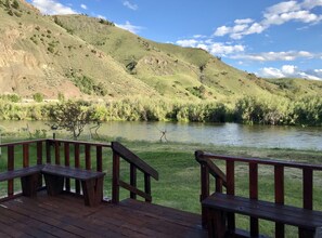 Une terrasse en bois avec des bancs, donnant sur une rivière et des collines.
