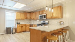 A modern kitchen with wooden cabinets, stainless steel appliances, a large island with stools, and pendant lighting. - Frances Cottage - Walking distance to downtown Saugatuck! Large backyard! (Saugatuck)