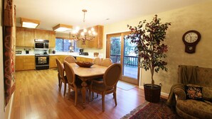 Une cuisine spacieuse avec des meubles en bois, une table à manger avec des chaises, un lustre et une grande plante en pot.