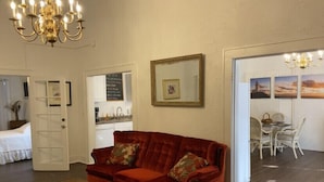 A living room with a red velvet sofa, a coffee table, a chandelier, a dining area with a table and chairs, and a kitchen visible through an open door. - Spacious 1/1 apartment near Stetson, sky diving, river, springs, racing, beaches (Deland)
