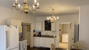 A modern kitchen with white cabinetry, a refrigerator, an oven, and a dining area with a table and chairs. - Spacious 1/1 apartment near Stetson, sky diving, river, springs, racing, beaches (Deland)