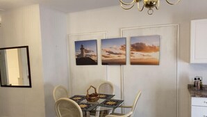 A dining area with a glass table, wicker chairs, and a chandelier. There are three framed pictures on the wall above the table. - Spacious 1/1 apartment near Stetson, sky diving, river, springs, racing, beaches (Deland)