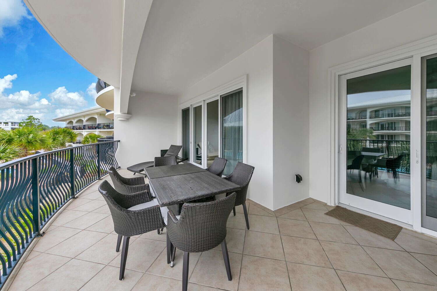 A balcony with a table and chairs, a glass door, and a view of a building with multiple balconies.
