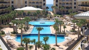 Een resort met een zwembad in het midden, meerdere balkons en palmbomen.