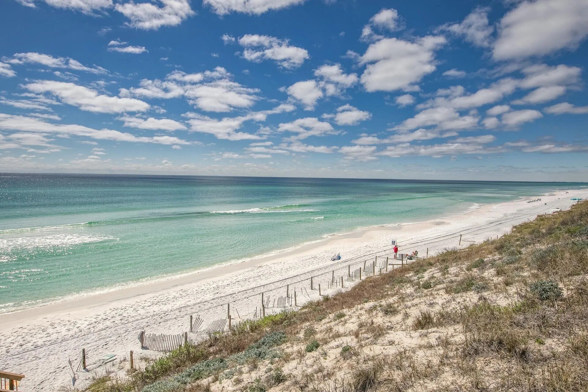 A beach with clear turquoise waters, a sandy shore, and a wooden fence running parallel to the beach.