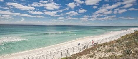 A beach with clear turquoise waters, a sandy shore, and a wooden fence running parallel to the beach.