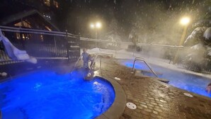 Un espace piscine extérieur chauffé, agrémenté d’un élément décoratif aquatique illuminé de lumière bleue, entouré d’un sol en briques et de rampes en métal.