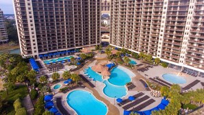 Ein Hochhaus-Hotel mit mehreren Swimmingpools, Liegestühlen und Palmen.