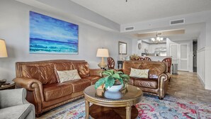 Ein Wohnzimmer mit zwei braunen Ledersofas, einem runden Couchtisch mit einer Pflanze, einem farbenfrohen Teppich und einem großen Gemälde, das einen blauen Himmel und ein Meer zeigt.