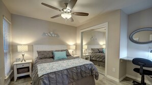 Quarto com uma cama, uma escrivaninha, uma cadeira, um ventilador de teto e um espelho.