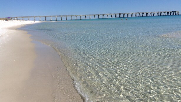 Una platja amb aigües poc profundes i cristal·lines i un llarg moll que s'endinsa al mar.