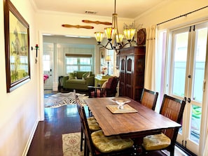 Un comedor con mesa de madera, sillas, una lámpara de araña y vista a una sala de estar a través de un umbral abierto.