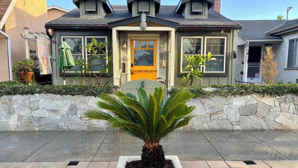 Una casa con un muro de piedra, una puerta amarilla y una planta en maceta al frente.