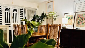 A dining area with a ceiling fan, a dining table with chairs, potted plants, and framed artwork on the wall.