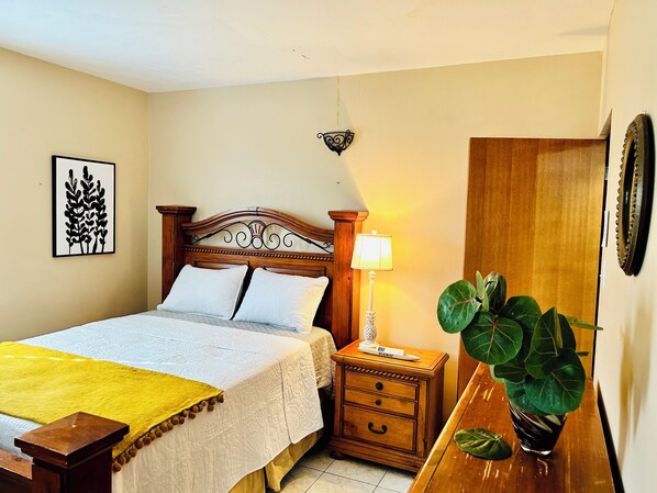 A neatly arranged bedroom with a bed, bedside table, lamp, and a potted plant. - Cultural Oasis: Beachfront Gem, Puerto Rican Heritage at Your Doorstep (Santa Isabel)