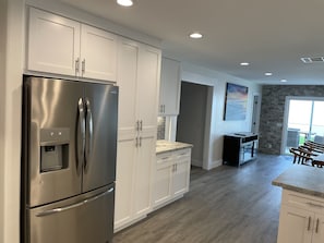 A modern kitchen with white cabinetry, a stainless steel refrigerator, and a stone backsplash. - Camp Pendleton Retreat with 7 person SPA 5bd 2 bath sleeps 12 (Oceanside)