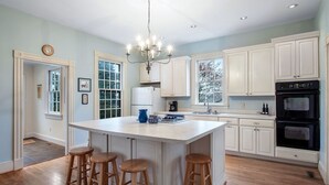 A kitchen with a central island, wooden stools, white cabinets, a chandelier, and a black oven. - Private Paradise -  Historic 1870 Home on 630 Acre Estate - Pool, Lake, Views (Goochland)