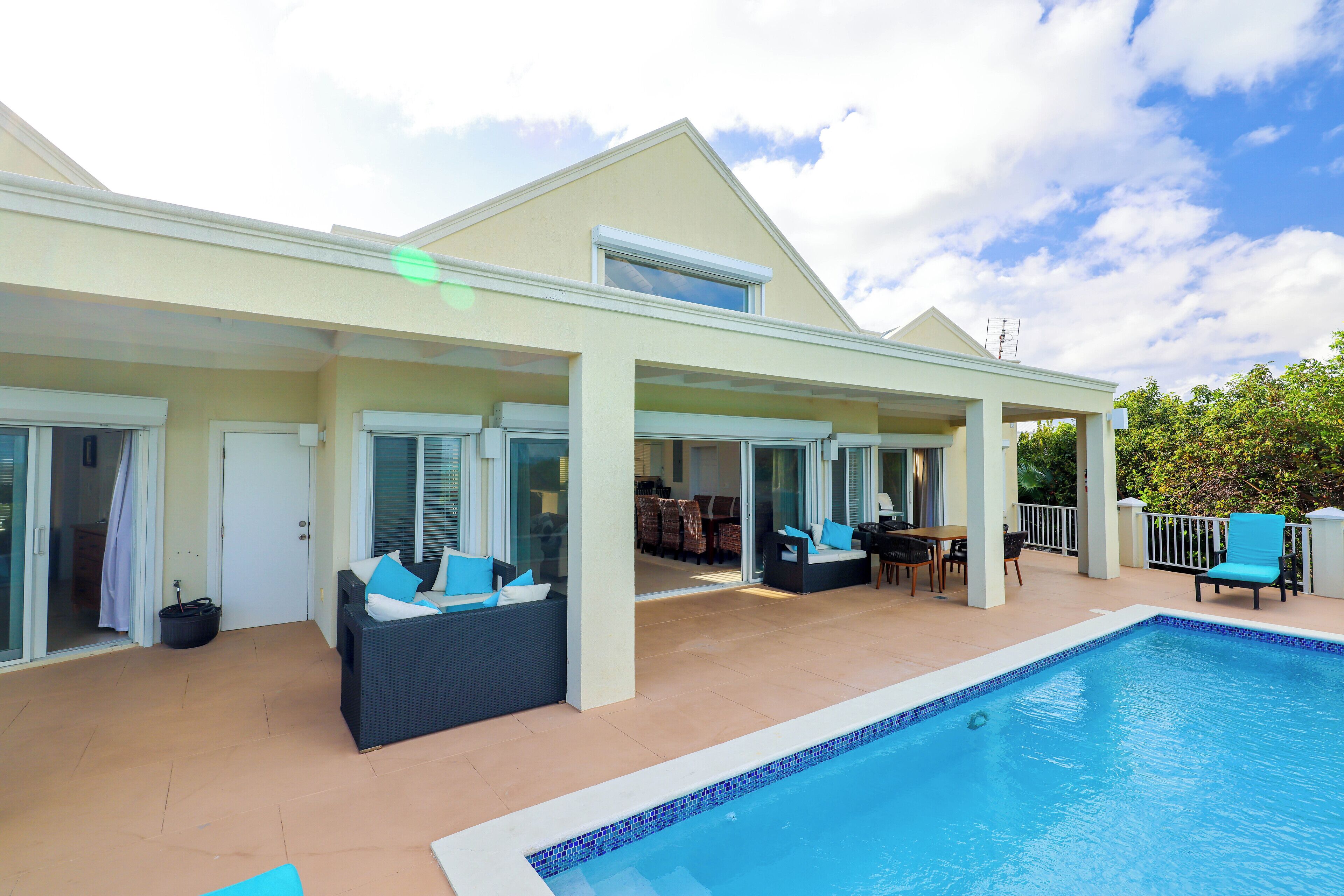 A covered outdoor area with a swimming pool, seating, and a patio with a table and chairs.