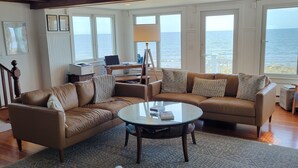 Un salon spacieux doté d’une grande fenêtre donnant sur la mer, d’une table basse ronde et d’un coin salon confortable.