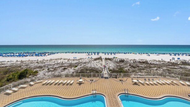 Un complexe hôtelier en bord de mer doté d’une piscine, de parasols et offrant une vue dégagée sur l’océan.