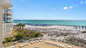Une vue sur la plage depuis un balcon, avec des chaises longues, une jetée et une plage de sable parsemée de parasols.