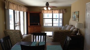 A dining area with a table and chairs, a television, and a ceiling fan. - Hobbie's Hideaway - Fall Dates Available (Gulf Shores)