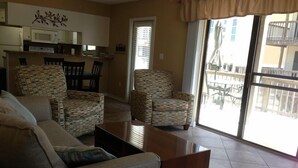 A living room with a sofa, two armchairs, a coffee table, and a view of the outside through large windows. - Hobbie's Hideaway - Fall Dates Available (Gulf Shores)