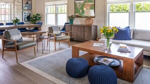 Ein modernes Wohnzimmer mit einem Holztisch, blauen Hocker, einer Couch und einem Essbereich mit einer Holzbank und Stühlen.