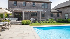 Ein zweistöckiges Haus mit einem Hinterhof, einer Terrasse, einem Swimmingpool und einem überdachten Sitzbereich im Freien.