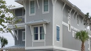 Une maison à deux étages dotée d’un balcon, de grandes fenêtres et d’un porche avant couvert.