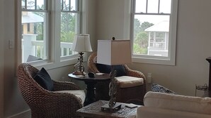 Un salon avec des meubles en osier, une table avec une lampe et de grandes fenêtres.