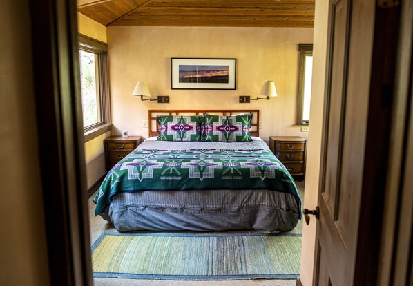 Une chambre à coucher comprenant un lit, deux tables de chevet, une commode, un tableau accroché au mur et une fenêtre.