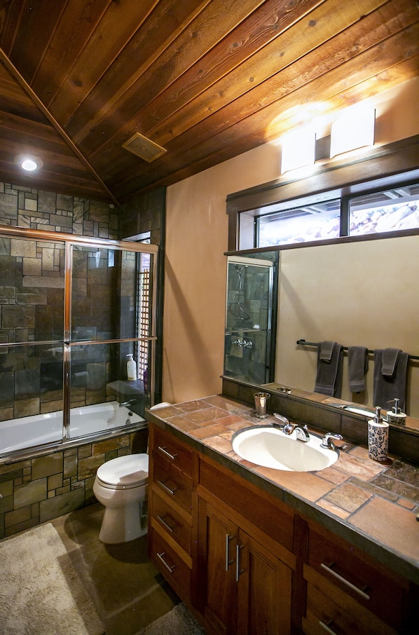 Un baño con ducha envuelta en vidrio, inodoro blanco, lavabo con espejo y armarios de madera.