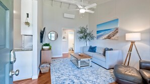 Sala de estar com sofá branco, mesa de centro, poltrona de couro, abajur e quadro de uma praia.