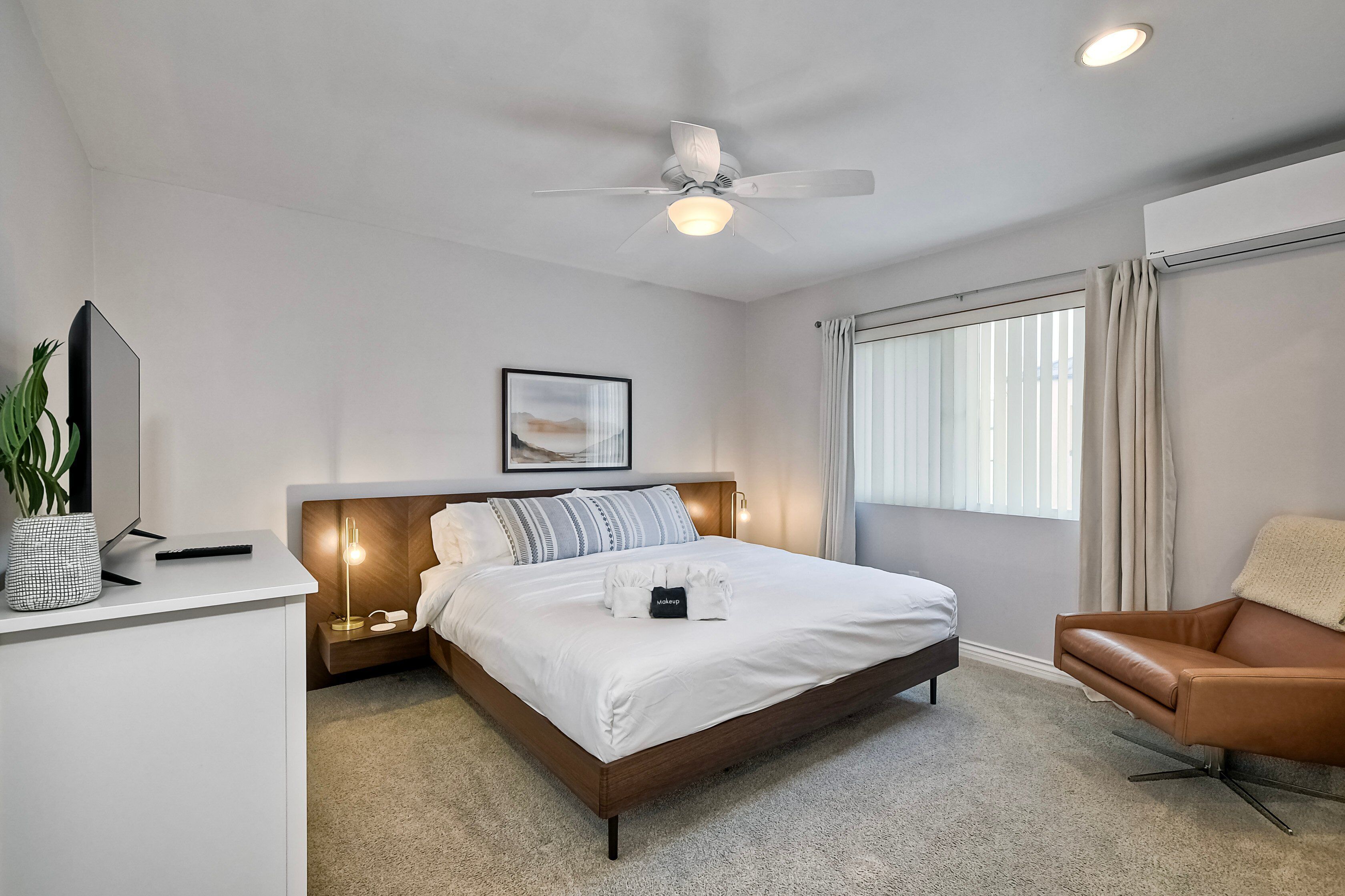 A modern hotel room with a large bed, bedside table, lamp, and a ceiling fan.