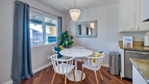 Uma sala de jantar com uma mesa redonda e quatro cadeiras, um candelabro, um espelho grande e vista para um edifício.